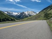 the road is paved with yellow markings and has a snowy mountain range in the background