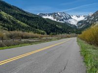 the road is paved with yellow markings and has a snowy mountain range in the background