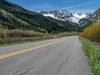 the road is paved with yellow markings and has a snowy mountain range in the background