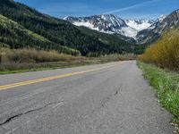 the road is paved with yellow markings and has a snowy mountain range in the background