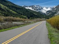 the road is paved with yellow markings and has a snowy mountain range in the background