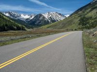 the road is paved with yellow markings and has a snowy mountain range in the background