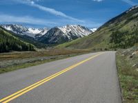 the road is paved with yellow markings and has a snowy mountain range in the background