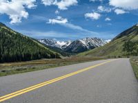 the road is paved with yellow markings and has a snowy mountain range in the background