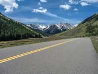 the road is paved with yellow markings and has a snowy mountain range in the background