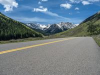 the road is paved with yellow markings and has a snowy mountain range in the background