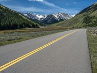 the road is paved with yellow markings and has a snowy mountain range in the background