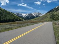 the road is paved with yellow markings and has a snowy mountain range in the background