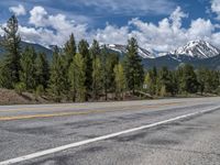 road in the mountains with pine trees and mountains in the background with blue sky with fluffy clouds