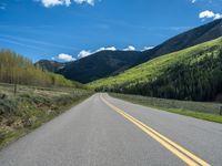 the road is paved with yellow markings and has a snowy mountain range in the background