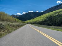 the road is paved with yellow markings and has a snowy mountain range in the background