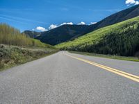 the road is paved with yellow markings and has a snowy mountain range in the background