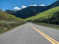 the road is paved with yellow markings and has a snowy mountain range in the background