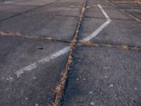 a paved parking lot in an industrial area, some have cracks on them and some have bare grass in the middle