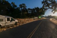 cars are driving down a paved street near the tall grass fields on an empty street