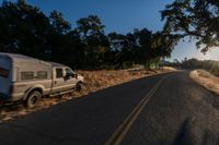 cars are driving down a paved street near the tall grass fields on an empty street