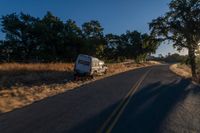 cars are driving down a paved street near the tall grass fields on an empty street