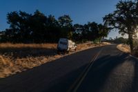 cars are driving down a paved street near the tall grass fields on an empty street