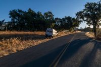 cars are driving down a paved street near the tall grass fields on an empty street