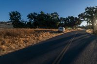 cars are driving down a paved street near the tall grass fields on an empty street