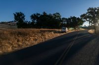 cars are driving down a paved street near the tall grass fields on an empty street