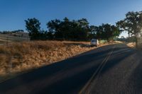 cars are driving down a paved street near the tall grass fields on an empty street