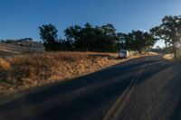 cars are driving down a paved street near the tall grass fields on an empty street