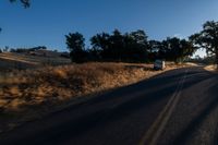 cars are driving down a paved street near the tall grass fields on an empty street