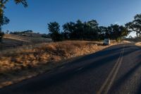 cars are driving down a paved street near the tall grass fields on an empty street