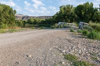 a rural dirt road in the countryside with an old bridge crossing the gravel lot on one side and a few trees near by