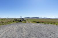 a dirt road with fence and a white vehicle behind it, in the distance, are hills