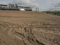 dirt track with some buildings and an event venue in the distance, in front of a field with a sky background