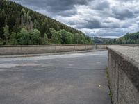 concrete walkway with trees and fenced in area on opposite sides of the road and one side of the road