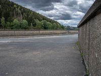 concrete walkway with trees and fenced in area on opposite sides of the road and one side of the road