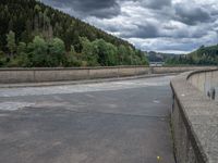 concrete walkway with trees and fenced in area on opposite sides of the road and one side of the road