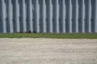the red hydrant stands on the corner of the street beside a steel building in a grassy field