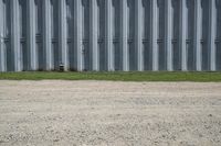 the red hydrant stands on the corner of the street beside a steel building in a grassy field