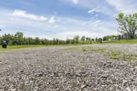 a empty lot on a sunny day with trees and some rocks around it and a green grassy area in the background