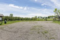 a empty lot on a sunny day with trees and some rocks around it and a green grassy area in the background