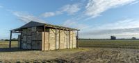 a small wooden structure with two doors on a farm with a cloudy sky above them