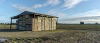 a small wooden structure with two doors on a farm with a cloudy sky above them