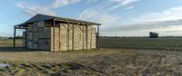 a small wooden structure with two doors on a farm with a cloudy sky above them