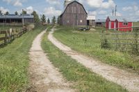 a farm yard with a dirt road leading into an old red barn and silo