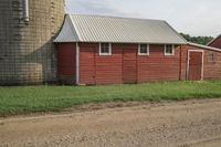 red barn with large windows is next to a green yard and silo with a few trees