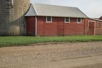 red barn with large windows is next to a green yard and silo with a few trees