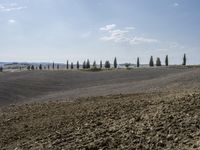 an empty rural field with rolling hills in the background under a partly cloudy blue sky