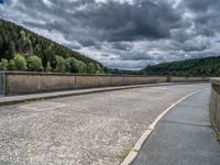 concrete walkway with trees and fenced in area on opposite sides of the road and one side of the road