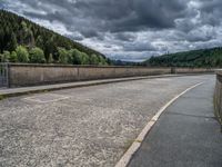 concrete walkway with trees and fenced in area on opposite sides of the road and one side of the road