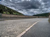 concrete walkway with trees and fenced in area on opposite sides of the road and one side of the road