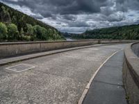 concrete walkway with trees and fenced in area on opposite sides of the road and one side of the road